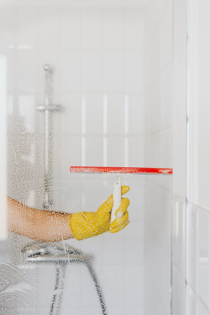 A person wiping a glass shower door with a squeegee