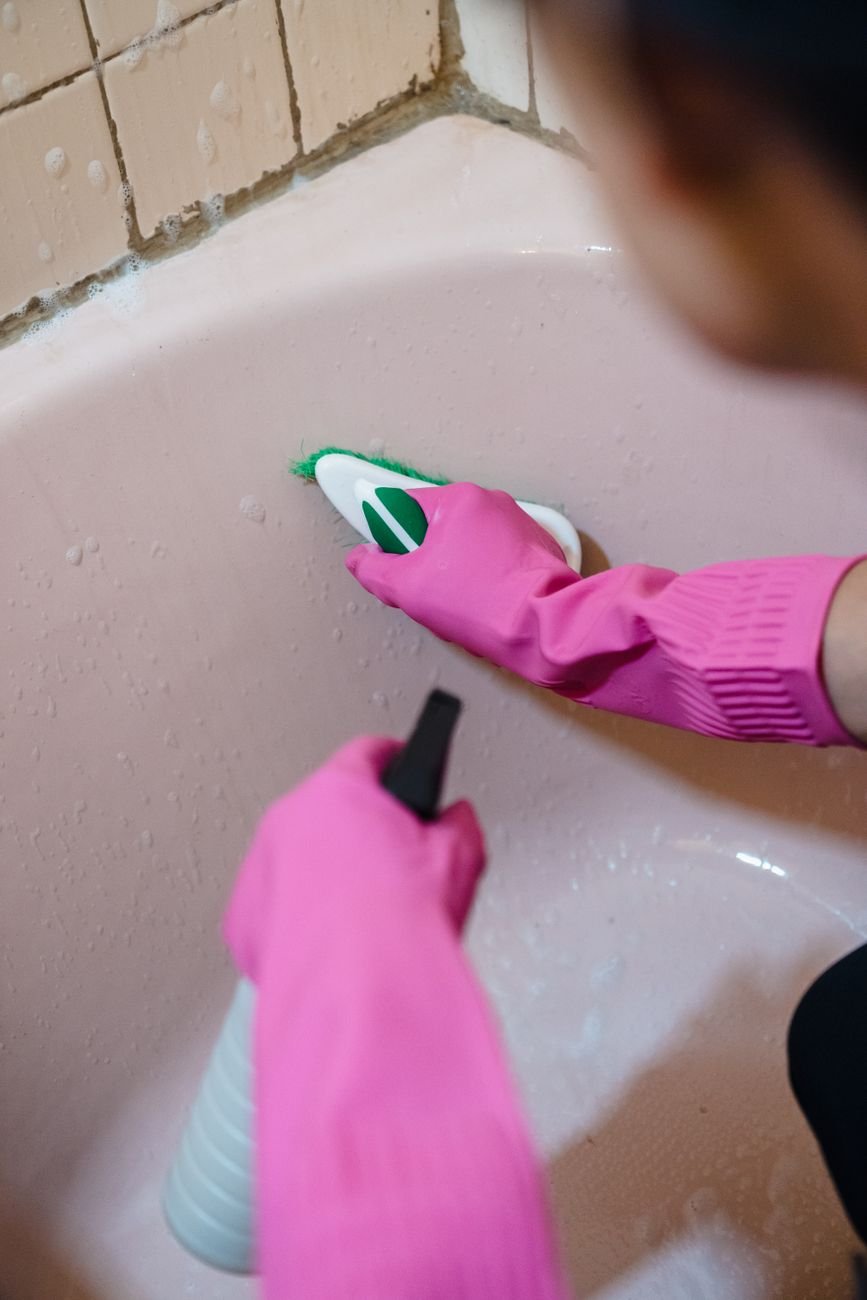 Gloved hands scrubbing a white bathtub