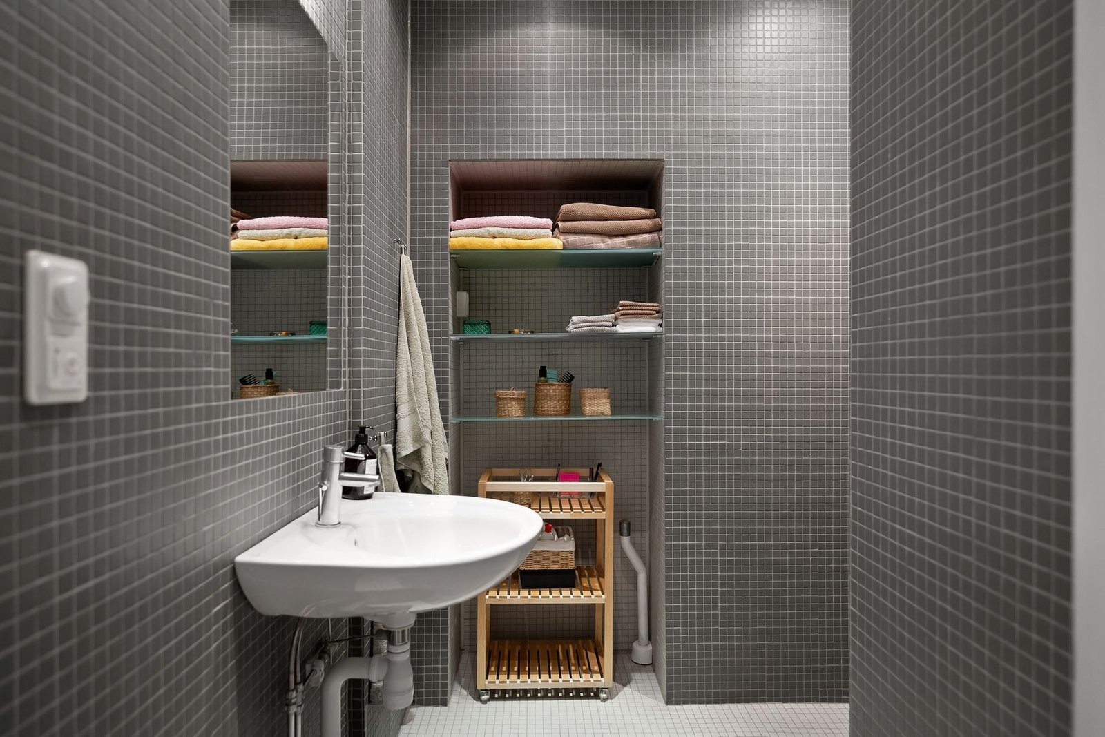 A small, tidy bathroom with towels and baskets on open shelves