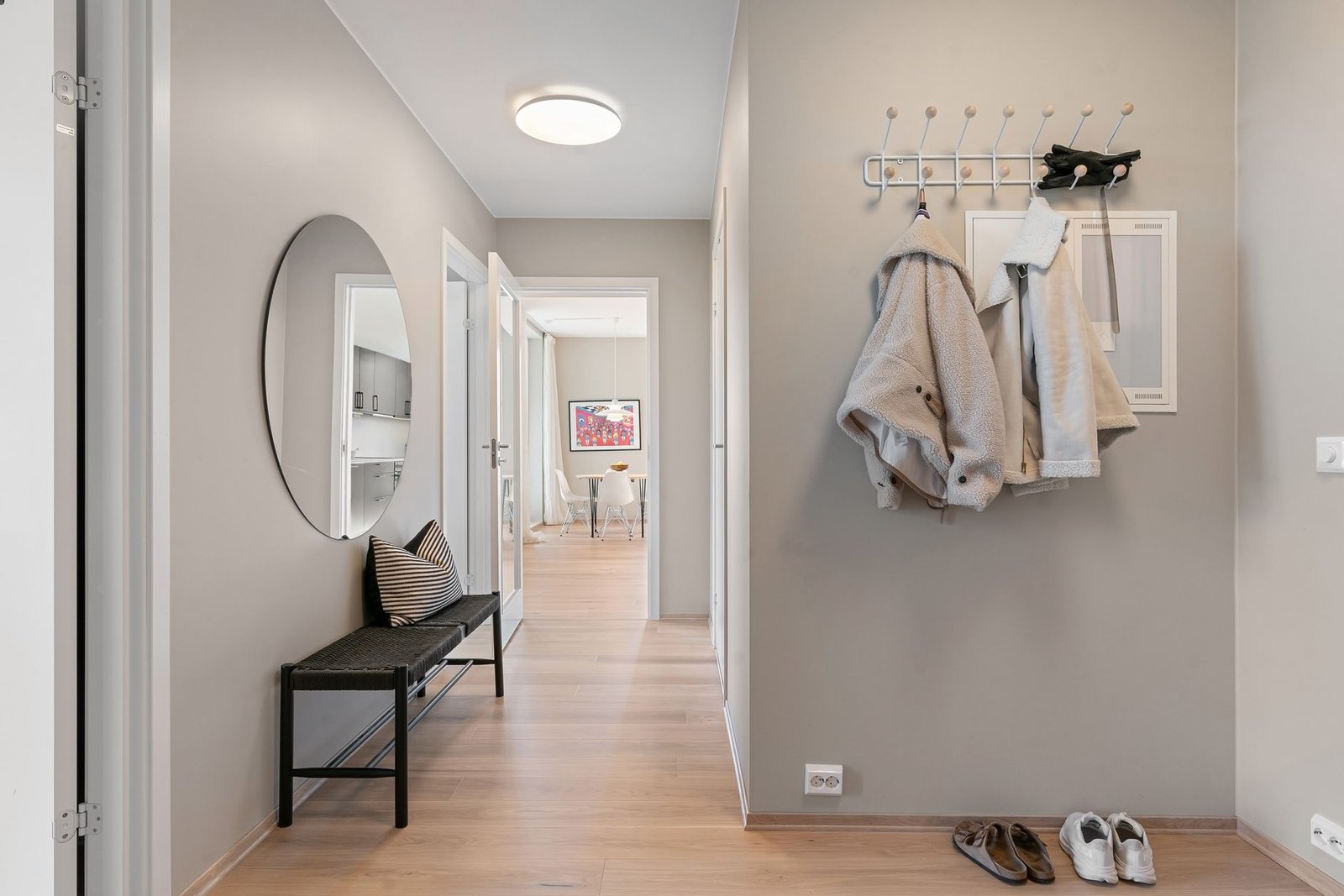 An organized entryway with coats on hooks, baskets and a dog leash hanging by the door