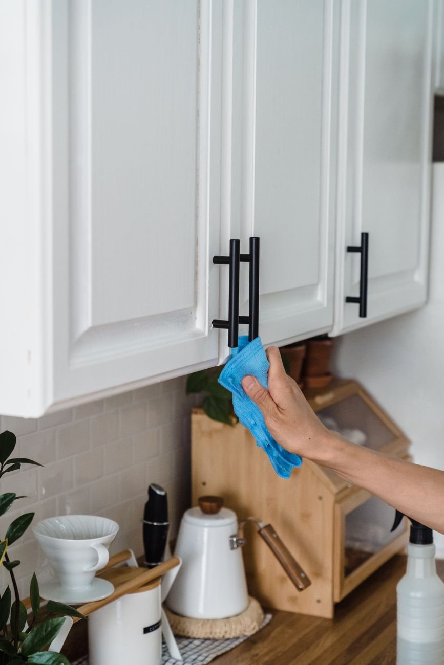 A person wiping down kitchen cabinets with a cloth