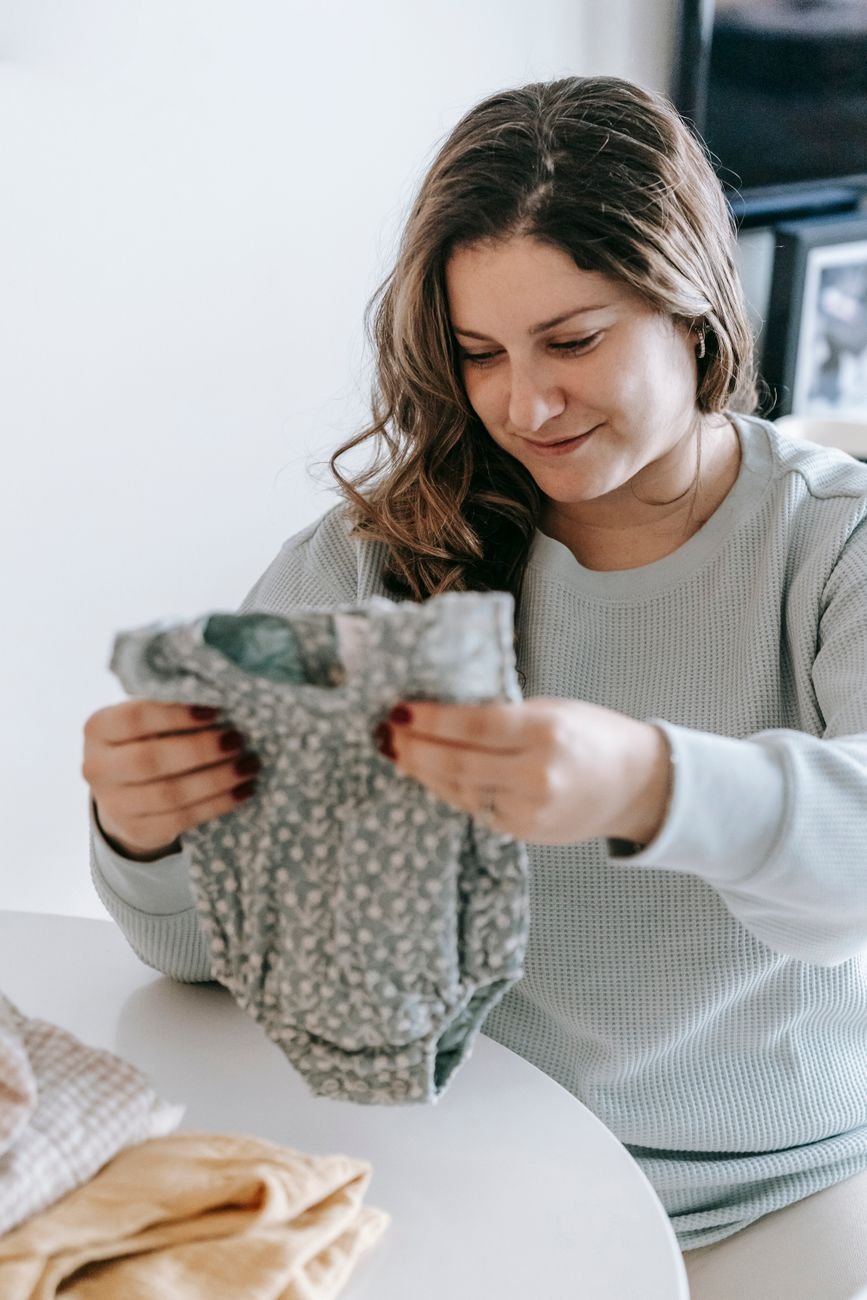 A pregnant woman folding tiny baby clothes
