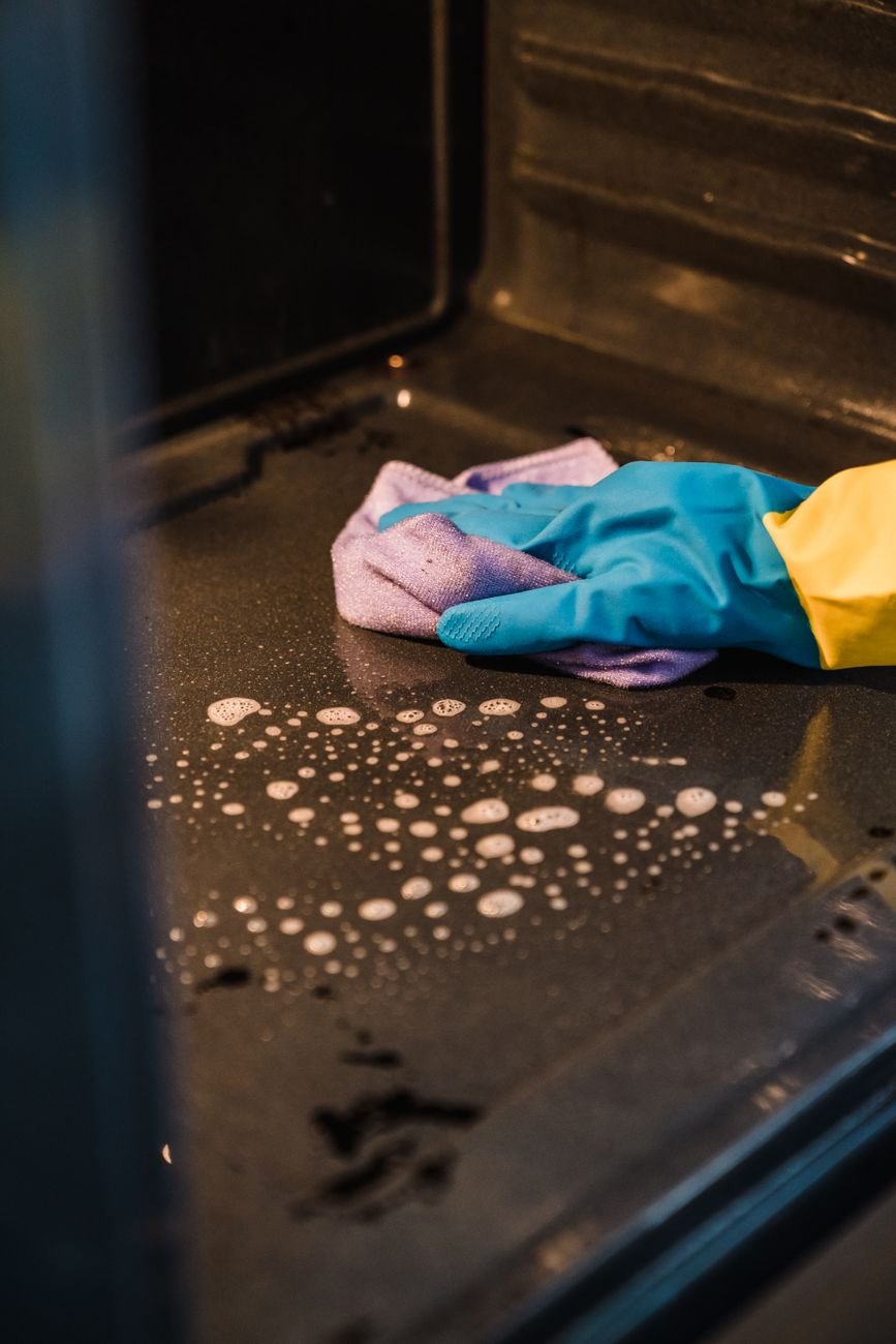A person in rubber gloves wiping the inside of an oven
