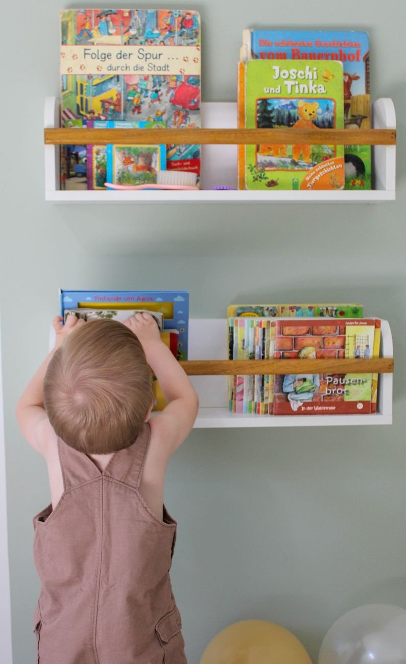 A toddler reaching for picture books on a low wall shelf